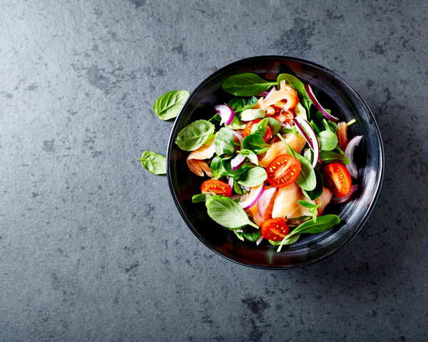 Salat mit Tomaten und Lachs auf grauem Tisch