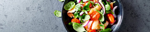 Salat mit Tomaten und Lachs auf grauem Tisch