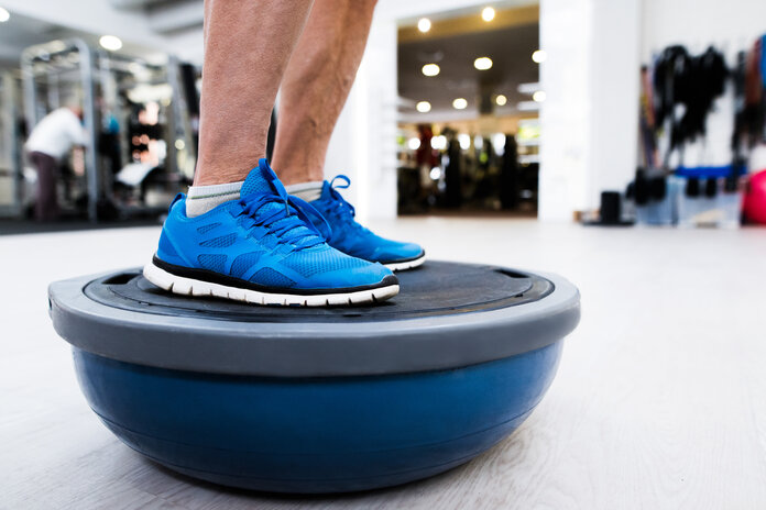 Eine Person macht Balanceübungen auf einem halbierten Ball im Trainingsraum der Physiotherapie.