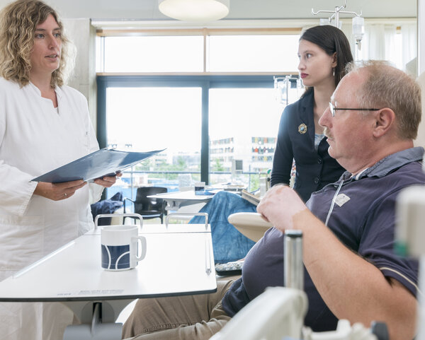 Ärztin spricht mit Patient und einer jungen Angehörigen, während der Patient ambulant eine Infusion erhält.