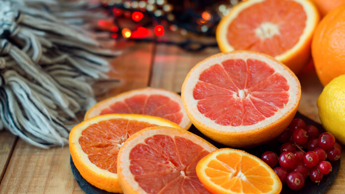 Grapefruit- und Orangenscheiben auf einer Platte, im Hintergrund Tannenzweige und eine leuchtende Lichterkette.