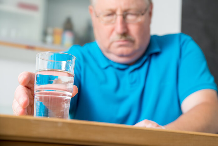 Ein Mann greift nach einem mit Wasser gefülltem Glas.