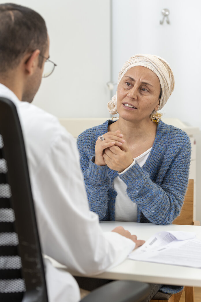 Frau mit Kopftuch und ihr behandelnder Arzt sitzen an einem Tisch und sprechen miteinander.