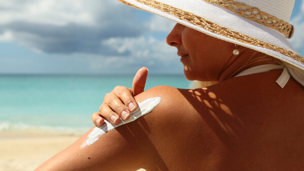 Frau mit Sonnenhut benutzt Sonnencreme am Strand.