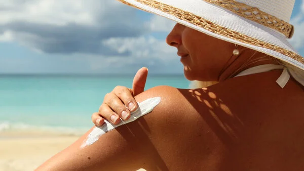 Sonnencreme-verwenden, © boophotography/Thinkstock Frau mit Sonnenhut benutzt Sonnencreme am Strand.