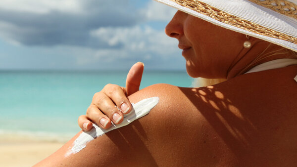 Frau mit Sonnenhut benutzt Sonnencreme am Strand.