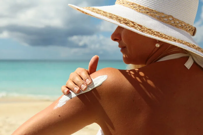 Sonnencreme-verwenden, © boophotography/Thinkstock Frau mit Sonnenhut benutzt Sonnencreme am Strand.