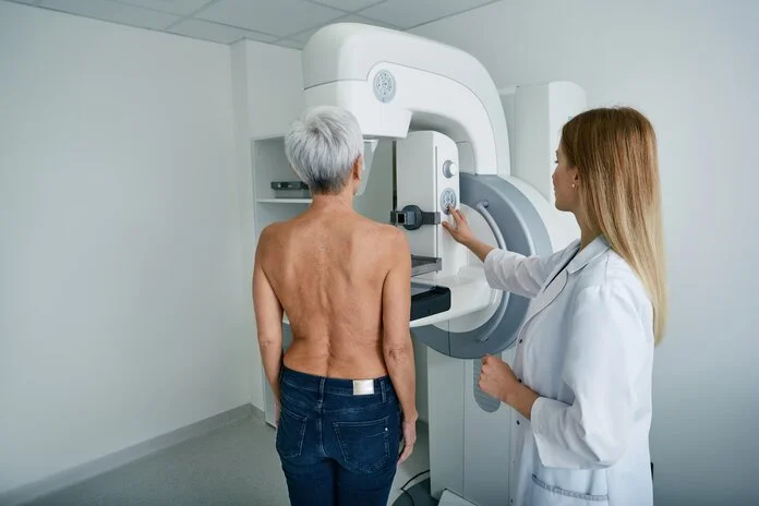 Ältere frau bei Mammographie, © Peakstock, Shutterstock Eine ältere Frau steht oberkörperfrei vor einem Mammographie-Gerät, neben ihr steht eine Röntgenassistentin.