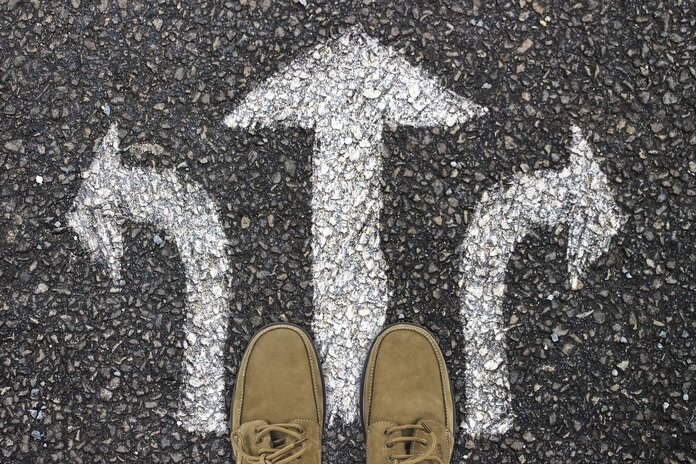 Füße stehen auf der Straße, davor sind 3 Pfeile auf die Straße gemalt, die nach vorn, rechts und links weisen.