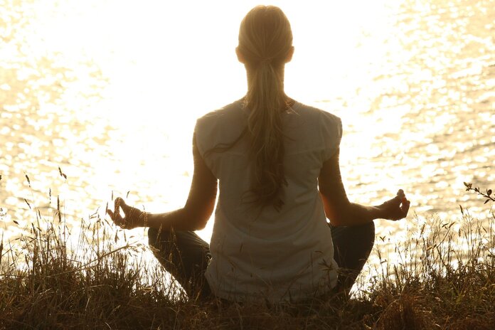 Silhouette einer meditierenden Frau im Schneidersitz am See (Rückenansicht).