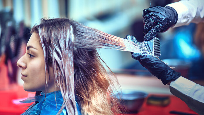 Junge Frau mit langen Haaren bekommt die Haare beim Friseur gefärbt mit chemischer Haarfarbe.