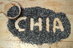 Chia-Samen liegen auf einem Holztisch, das Wort "Chia" wurde mit dem Finger in den Haufen Chia-Samen geschrieben.