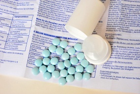 Auf einem Beipackzettel legen blaue Tabletten neben einer geöffneten Tablettenflasche.