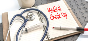 Auf der rechten Seite eines aufgeschlagenen Ringbuchs steht in roter Schrift "Medical Check Up", auf der linken Seite liegen ein Stetoskop und eine Spritze.